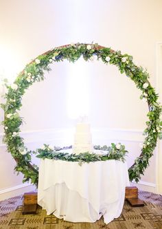 a wedding cake on top of a table surrounded by greenery and flowers in a circle