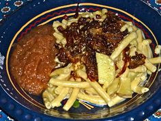 a blue plate topped with pasta and meat covered in sauce next to french fries on top of a table