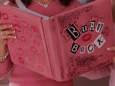 a woman is holding a pink book with the words burn book written in black on it