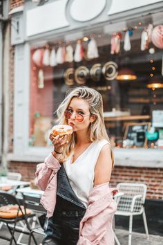 a woman eating food in front of a storefront with tables and chairs behind her