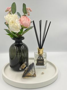 a black vase filled with flowers and reeds on top of a white tray next to a bottle of perfume