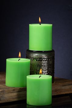 three green candles sitting on top of a wooden table