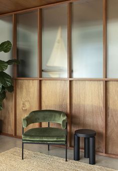 a green chair sitting on top of a rug next to a wooden wall with glass doors