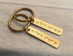 two personalized brass keychains with names and date engraved on the sides, sitting on a gray blanket