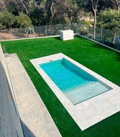 an artificial swimming pool in the middle of a backyard with grass and fence around it