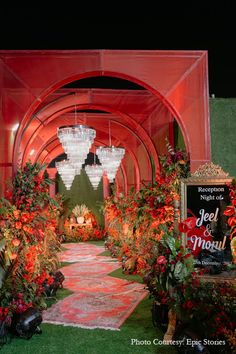 an outdoor event with red and green decorations on the grass, chandeliers hanging from the ceiling