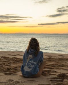 a woman sitting on the beach watching the sunset