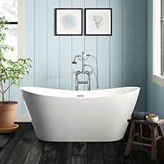 a white bath tub sitting next to a wooden floor in a blue bathroom with two pictures on the wall