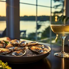 a plate of oysters next to a glass of wine on a table with water in the background