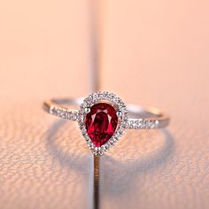 a ring with a heart shaped red stone surrounded by white diamonds on a pink surface