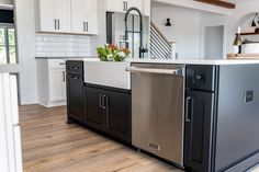 a kitchen with black and white cabinets, stainless steel dishwasher, and wood flooring