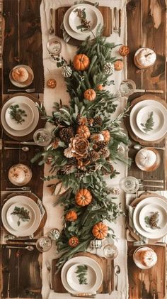 the table is set with white plates, silverware and pine cones on it's centerpieces