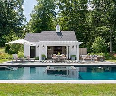 a pool house with an outdoor kitchen and dining area next to the swimming pool is surrounded by lush green trees