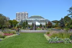 people are walking around in the park with many flowers and greenery on both sides