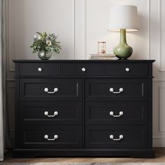 a black dresser with white drawers and a green vase on top