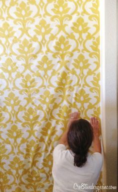 a woman is painting a wall with yellow and white damasks on the walls