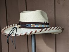 Levi starts with a Mexican soft palm leaf hat body that has a 3 3/4" brim and 5 1/4" crown. Hand laced in chocolate brown Kangaroo leather lace. The beaded hatband has colors of white, red, orange and turquoise and is mounted on dark brown suede. The back of the band has a deer antler bead for accent. Old Silver Concho with 3 horse heads and decorative feathers completes the hat. Brown High Crown Hat With Adjustable Fit, Brown Adjustable High Crown Hat, Custom Brown Hat Bands For Kentucky Derby, Custom Brown Hat Band For Kentucky Derby, Brown High Crown Hat Bands For Country Events, Brown High Crown Hat Band For Country Events, Adjustable Hand Tooled Brown Hats, Adjustable Brown Hand Tooled Hat, Adjustable Hand-tooled Brown Hat