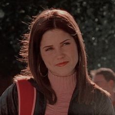 a woman with brown hair wearing a pink shirt and black jacket is looking at the camera