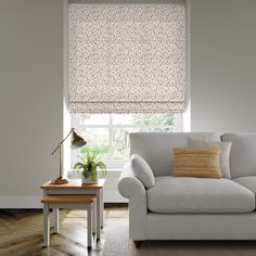 a living room with a couch, table and window covered in roman blind shades on the windowsill