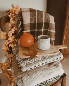 a stack of blankets and a cup on a wooden table next to an orange pumpkin