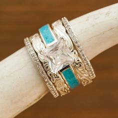 a ring with a princess cut diamond and turquoise stone in the center on a wooden stick