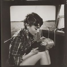 a black and white photo of a woman sitting on a boat looking at something in her hand