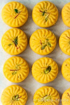 twelve yellow cakes are arranged on a white counter top, with green leaves sticking out of them