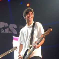 a young man holding two bass guitars on stage