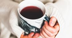 a person holding a cup of tea in their left hand and wearing a white sweater