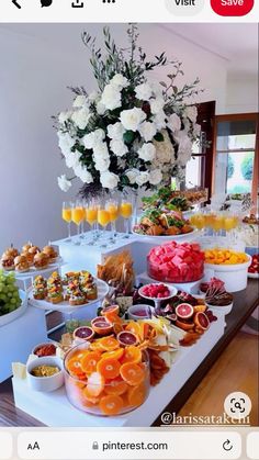 an assortment of fruits and snacks on a buffet table with flowers in the background at a wedding reception