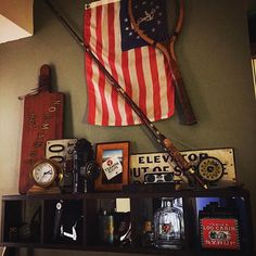 an american flag hanging on the wall above a shelf with various antiques and other items