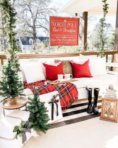 the porch is decorated for christmas with red and white pillows, plaid blankets, and trees