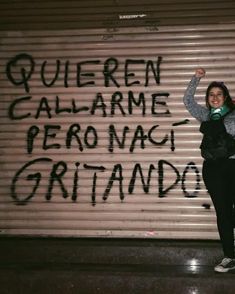 a woman standing in front of a garage door with graffiti written on the wall behind her