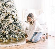 a woman sitting on the floor next to a christmas tree with gold and white ornaments