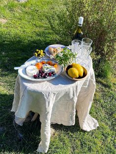 a table with plates and bowls of food on it in the grass next to a bottle of wine