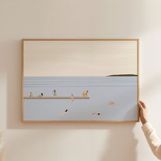 a person holding up a painting with people on the beach in water and birds flying around