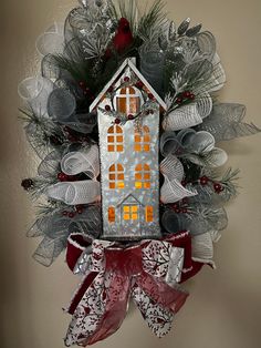 a christmas wreath with a house hanging on it's side and red ribbon around the front