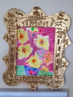 a painting is hanging on the wall in a gold frame with flowers painted on it