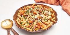 a bowl filled with pasta and vegetables on top of a white table next to two spoons