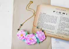 a necklace with pink flowers on it next to an old book and a gold chain