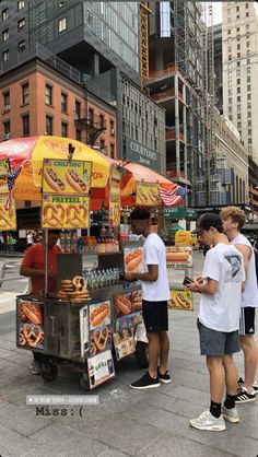 three young men standing in front of a hot dog stand on the side of a street