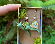 a person holding up a box with two small earrings in it's hand and moss growing on the inside