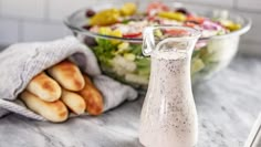 a salad with dressing in a glass bottle next to a bowl of breadsticks