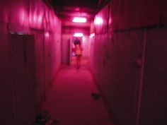 a woman is walking down a long hallway with pink lights on the walls and floor