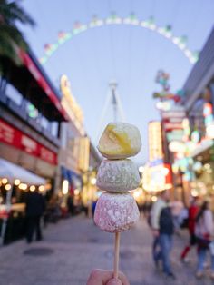 a person holding up some food on a stick in front of a ferris wheel at night