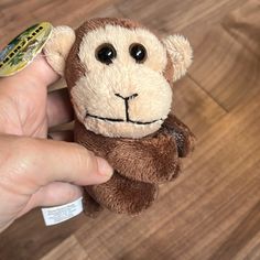 a hand holding a small stuffed monkey on top of a wooden floor next to a sticker