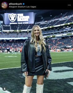 a woman standing on top of a football field wearing boots and a leather jacket with her hands in her pockets