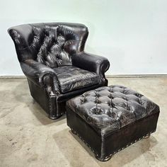 a black leather chair and foot stool in an empty room