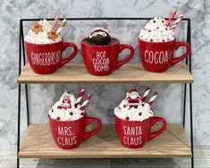 three red mugs filled with hot chocolate and marshmallows on top of a wooden shelf