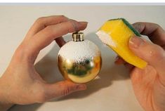 two hands are holding a yellow and white christmas ornament with a sponge on it